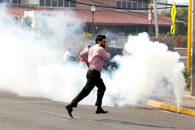 A pedestrian covers his nose as he runs past a tear gas canister fired by police during a protest to demand justice over the murder of environmental and indigenous rights activist Berta Caceres in Tegucigalpa, Honduras, May 9, 2016. (Photo by Jorge Cabrera/Reuters)