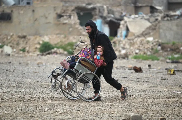 An Iraqi man pushes a girl on a wheelchair as they flee the al- Abar neighbourhood in west of Mosul, while Iraqi forces battle against Islamic State (IS) group jihadist to recapture the city, on April 13, 2017. (Photo by Ahmad Al-Rubaye/AFP Photo)