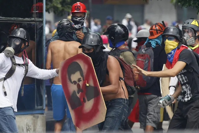 An anti-government protester holds a homemade shield featuring a defaced image of President Nicolas Maduro during a student march blocked by security forces from reaching the Eduction Ministry in Caracas, Venezuela, Monday, May 8, 2017. The protest movement against President Nicolas Maduro, that has drawn masses of people into the streets nearly every day since March, has left some three dozen dead. (Photo by Ariana Cubillos/AP Photo)