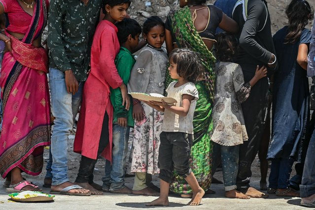 A child carries a plate after receiving free food being distributed as a charity by volunteers along a street in Hyderabad on July 11, 2024. (Photo by Noah Seelam/AFP Photo)