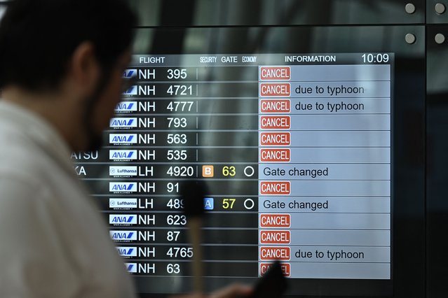 A TV news crew team works in front of a screen showing cancelled flights at the departure hall of Tokyo's Haneda Airport on August 16, 2024 as Typhoon Ampil barrels towards Japan's capital. (Photo by Philip Fong/AFP Photo)