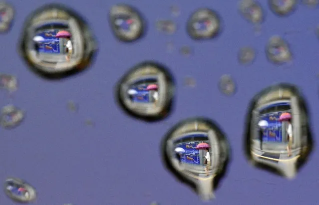 An image rotated 180 degrees shows raindrops on a car window reflecting pedestrians walking past a stock market indicator board in Tokyo, Japan, 13 June 2016. Japan's stocks dropped sharply due to a stronger yen and worries on the “Brexit” possibility. The benchmark Nikkei 225 Stock Average lost 582.18 points, or 3.51 percent, to close at 16,019.18. (Photo by Franck Robichon/EPA)