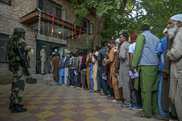 An Indian security personnel stands guard as voters queue up to cast their ballots at a polling station during the first phase of assembly elections in Pulwama, south of Srinagar on September 18, 2024. Indian-administered Kashmir began voting on September 18 in the first local elections since the cancellation of its special semi-autonomous status sparked fury in the troubled Himalayan territory, which is also claimed by Pakistan. (Photo by Tauseef Mustafa/AFP Photo)