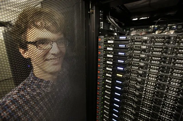 In this Wednesday, June 22, 2016, photo, Massachusetts Institute of Technology researcher Carl Vondrick looks through a protective door while standing next to a computer server cluster, right, on the MIT campus, in Cambridge, Mass. MIT says a computer that binge-watched TV shows such as “The Office”, “Big Bang Theory” and “Desperate Housewives” learned how to predict whether the actors were about to hug, kiss, shake hands or slap high-fives, a breakthrough that eventually could help the next generation of artificial intelligence function less clumsily. (Photo by Steven Senne/AP Photo)
