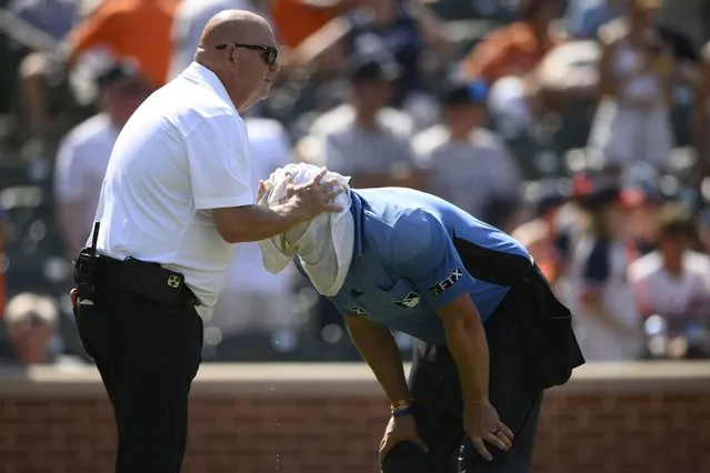 Baltimore Orioles head trainer Brian Ebel, left, helps home plate umpire Scott Barry get relief with a wet towel around his head after the sixth inning of a baseball game between the Orioles and the New York Yankees, Sunday, July 24, 2022, in Baltimore. The Yankees won 5-0. (Photo by Nick Wass/AP Photo)