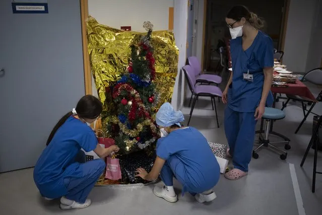 Hospital workers place gifts under a christmas tree in the COVID-19 intensive care unit at la Timone hospital in Marseille, southern France, Friday, December 24, 2021. Marseille's La Timone Hospital, one of France's biggest hospitals, has weathered wave after wave of COVID-19. On Christmas Eve, medical personnel decorated a fir tree in the corridor and seized a moment for a communal meal in their scrubs, trying to maintain a semblance of holiday spirit in between rounds. (Photo by Daniel Cole/AP Photo)