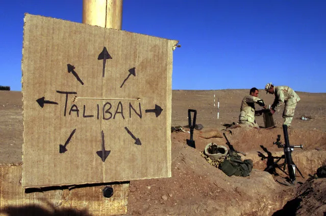 US Marines from Charlie 1/1 of the 15th MEU (Marine Expeditionary Unit) fill sand bags around their light mortar position on the front lines of the US Marine Corps base in southern Afghanistan December 1, 2001 nearby a cardboard sign reminding everyone that the Taliban forces could be anywhere and everywhere. This sign is one of several at an area that Charlie Company named Camp Justice on the perimiter of the larger base. (Photo by Jim Hollander/Reuters)