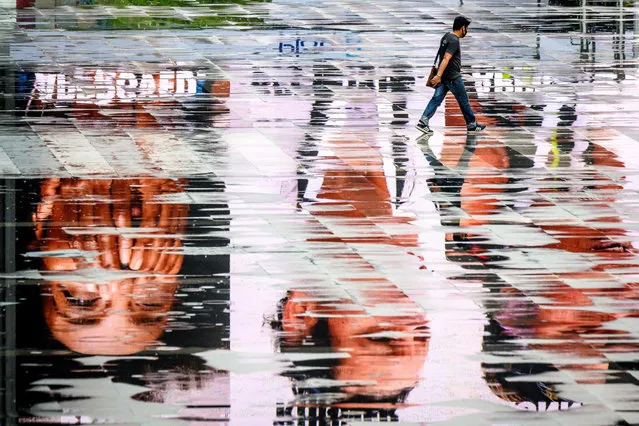 A man wearing a facemask, amid concerns over the spread of the COVID-19 coronavirus, walks among puddles reflecting advertisement screens on an empty square in Bangkok on March 15, 2020. (Photo by Mladen Antonov/AFP Photo)