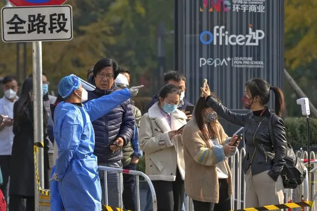 A woman, right, wearing a face mask shows her health check QR code as she and others line up to get their routine COVID-19 throat swabs at a coronavirus testing site in Beijing, Tuesday, November 8, 2022. Police in northeastern China say seven people have been arrested following a clash between residents and authorities enforcing COVID-19 quarantine restrictions. (Photo by Andy Wong/AP Photo)