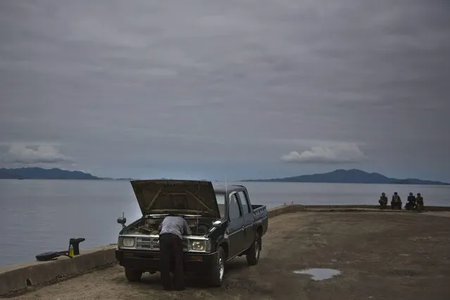In this June 21, 2014 photo, a man works on his car as others sit next to the sea Wonsan, North Korea. (Photo by David Guttenfelder/AP Photo)