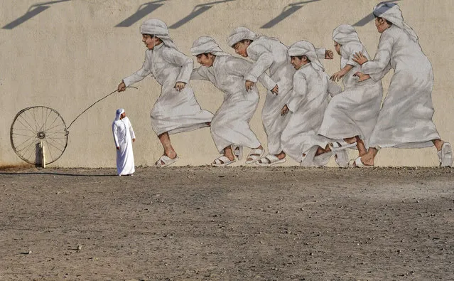 A man walks past a giant mural depicting boys running after a wheel, in Dubai on November 30, 2017. (Photo by Giuseppe Cacace/AFP Photo)