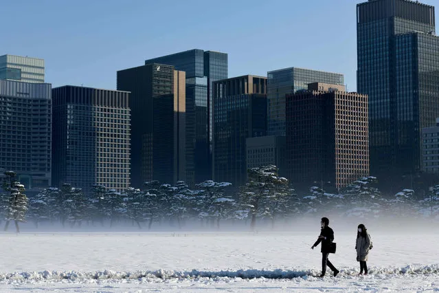 People walk across the snow covered ground near the Imperial Palace in Tokyo on January 23, 2018. Tokyo woke up to snow across the city a day after heavy snowfall and icy conditions injured dozens of people, grounded flights and paralysed some train services on January 22 after Japan' s weather agency issued its first snow warning for the city in four years. (Photo by Toshifumi Kitamura/AFP Photo)