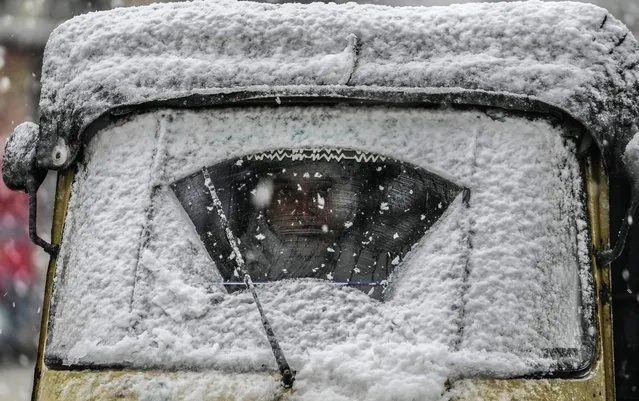 An auto driver looks through a snow-covered windshield in Srinagar, Indian controlled Kashmir, Friday, January 13, 2023. Kashmir region received fresh snow on Friday, affecting air and vehicular traffic. (Photo by Mukhtar Khan/AP Photo)