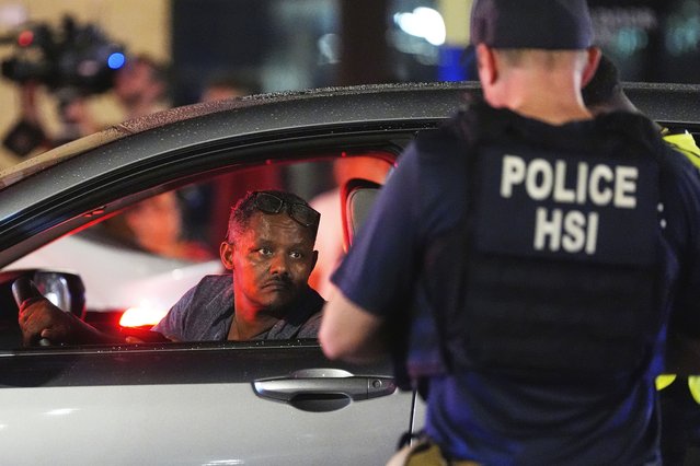 A driver peers from his window while a Department of Homeland Security agent and a city police officer conduct a traffic checkpoint along 14th Street in Washington, August 13, 2025. (Photo by Alex Brandon/AP Photo)