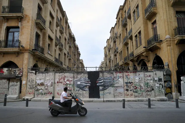 A man rides his scooter pasts a concrete wall that installed by security forces to don't let the anti-government protesters reach the parliament building, in downtown Beirut, Lebanon, Monday, October 12, 2020. A year ago, hundreds of thousands of Lebanese took to the streets in protests nationwide that raised hopes among many for a change in a political elite that over that decades has run the country into the ground. (Photo by Bilal Hussein/AP Photo)