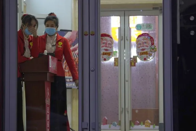 Chinese workers wait for customers at the entrance to a restaurant in Beijing on Sunday, December 27, 2020. China urges migrant workers not to travel home during February's Lunar New Year holiday to prevent further virus spread. (Photo by Ng Han Guan/AP Photo)