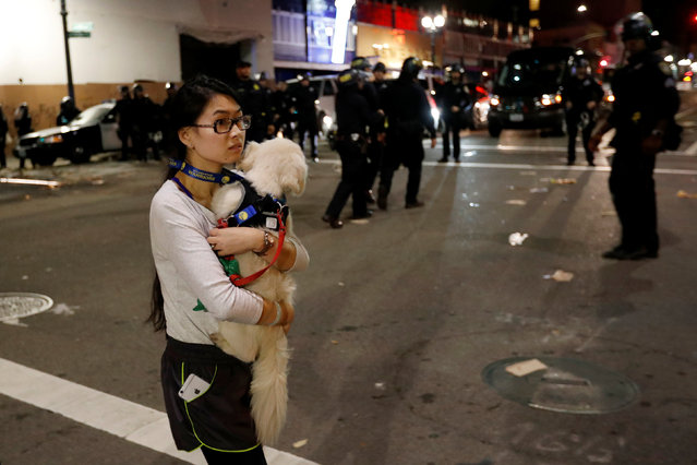 A pedestrian carries her dog as she walks by a line of police officers in riot gear during a demonstration in Oakland, California, U.S. following the election of Donald Trump as President of the United States November 9, 2016. (Photo by Stephen Lam/Reuters)