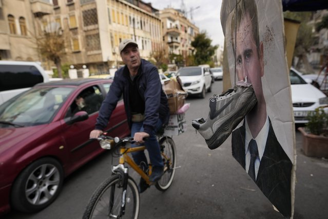 A cyclist rides past a portrait of ousted Syrian President Bashar Assad with a shoe attached to it as a sign of disdain, in Damascus, Syria, Monday, December 23, 2024. (Photo by Hussein Malla/AP Photo)