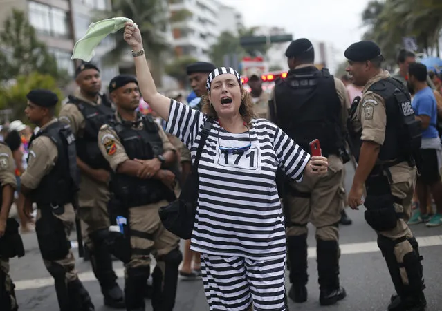 A reveler dressed in a jailbird costume sings aloud, backdropped by a Brazilian police unit during the Banda de Ipanema carnival parade in Rio de Janeiro, Brazil, Saturday, January 31, 2015. (Photo by Silvia Izquierdo/AP Photo)