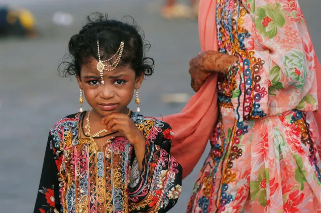 A girl adorned with jewelry wears a traditional dress while walking with her sibling during Eid al-Fitr celebrations, at Clifton beach in Karachi, Pakistan on June 18, 2018. (Photo by Akhtar Soomro/Reuters)