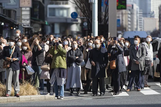 Some of the bystanders waiting at a traffic intersection take pictures of a clock on a building when the 10th annual tribute started at 2:46 p.m. for the victims of a 2011 disaster in Tokyo Thursday, March 11, 2021. Japan is marking the 10th anniversary Thursday of the earthquake, tsunami and nuclear disaster that hit the northeastern region. (Photo by Hiro Komae/AP Photo)