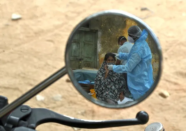 A health worker takes a nasal swab sample of a woman to test for COVID-19 are reflected in a mirror of a motorcycle in Hyderabad, India, Friday, May 7, 2021. (Photo by Mahesh Kumar A./AP Photo)