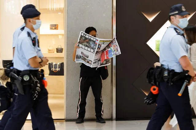 Police patrol past an Apple Daily supporter as he reads the final edition of the newspaper at a shopping mall in Hong Kong, China on June 24, 2021. (Photo by Tyrone Siu/Reuters)