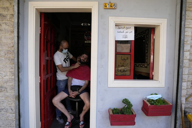 A Lebanese barber shaves the beard of a customer at the door of his shop during a power outage in a southern suburb of Beirut, Lebanon, Wednesday, August 11, 2021. Lebanon, which is mired in multiple crises including a devastating economic crisis, has faced months of severe fuel shortages that have prompted long lines at gas stations and plunged the small country, dependent on private generators for power, into long hours of darkness. Sign on door says, “Forbidden to enter without mask”. (Photo by Hassan Ammar/AP Photo)