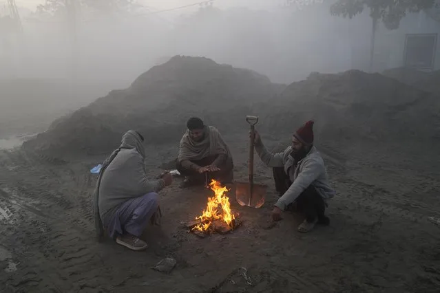 Laborers warm themselves around a fire while heavy fog envelopes the area in Lahore, Pakistan, Thursday, December 14, 2023. Various cities in eastern and central Pakistan continue to experience heavy fog, disrupting air and road transportation. (Photo by K.M. Chaudary/AP Photo)