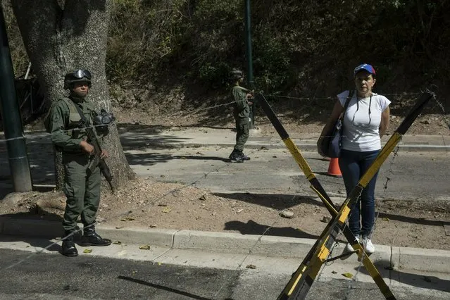A woman stands next to soldiers as other members of the opposition hand out copies of an amnesty law near Ft. Tiuna military base in Caracas, Venezuela, Sunday, January 27, 2019. Opposition National Assembly leader Juan Guaido, who declared himself interim president, said Friday that he would release the text of an existing amnesty law that would pardon members of the military who cooperate in restoring democracy and asked Venezuelans to share it with officers they know. (Photo by Rodrigo Abd/AP Photo)