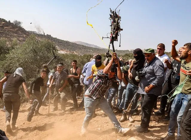 A Palestinian protester smashes an Israeli drone that reportedly fell because of a technical failure, during a demonstration against settlements in the West Bank village of Beita, on October 1, 2021. (Photo by Jaafar Ashtiyeh/AFP Photo)