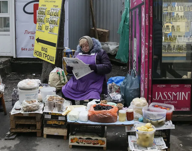 A woman reads a newspaper and waits for customers as she sells home made products near a currency exchange office in Kiev, Ukraine, March 3, 2016. (Photo by Gleb Garanich/Reuters)