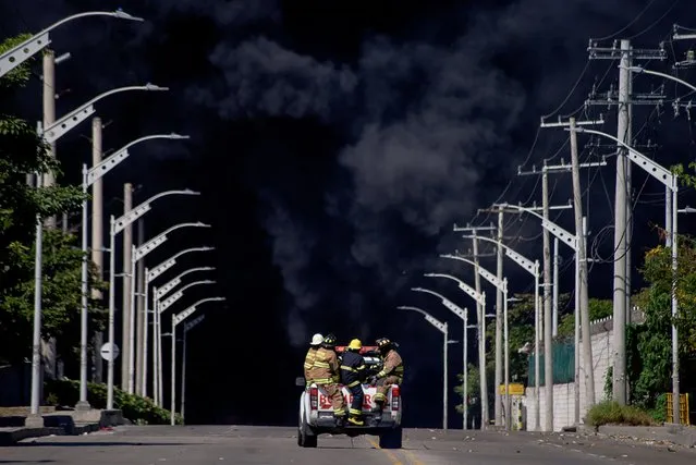 Firefighters are transported in a car as black smoke rises during a fire in a hydrocarbon storage area of the Bravo Petroleum company in Barranquilla, Colombia on December 21, 2022. (Photo by Charlie Cordero/Reuters)