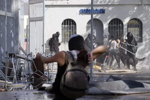 Protesters recover after being hit by a jet of water from a police operated water cannon at the University of Santiago, during clashes between students and police, in Santiago, Chile, Thursday, May 14, 2015. (Photo by Luis Hidalgo/AP Photo)