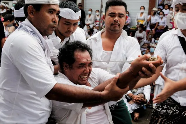 A Balinese Hindu man attempts to stab his forehead with a traditional Keris dagger during the sacred Ngerebong ritual in Bali, Indonesia on November 28, 2021. (Photo by Johannes P. Christo/Reuters)