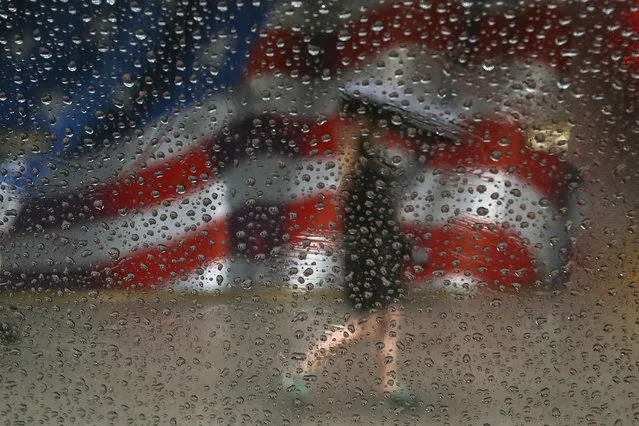 A woman walks with an umbrella in the rain past a U.S. flag painted on a building in the Manhattan borough of New York, February 16, 2016. (Photo by Carlo Allegri/Reuters)