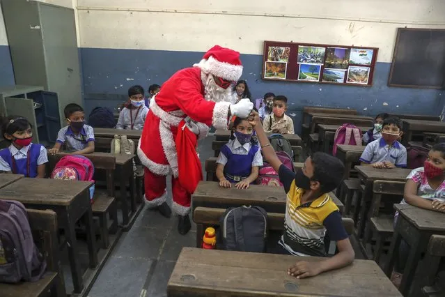 A man dress as Santa Claus greets students with a fist bump as they prepare to attend classes at a school in Mumbai, India, Wednesday, December 15, 2021. After being closed for nearly-20-months due to the coronavirus pandemic, schools in Mumbai reopened for classes 1 to 7 Wednesday. (Photo by Rafiq Maqbool/AP Photo)