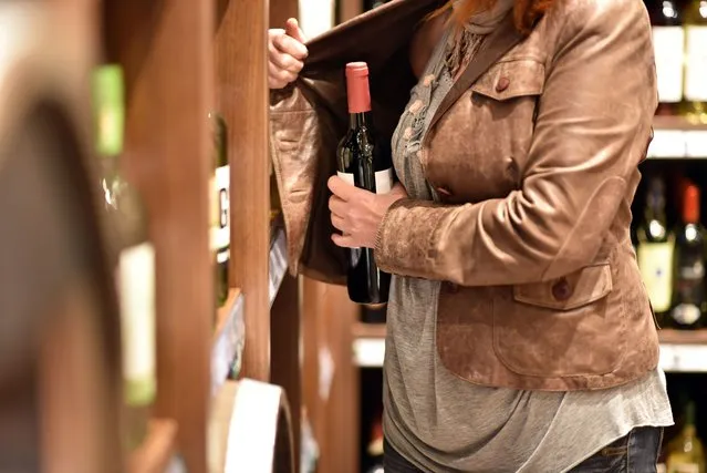 A woman steals a bottle of wine in a supermarket. (Photo by industryview/Getty Images)