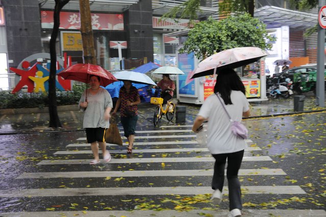 Pedestrians, holding umbrellas, cross a street amid a rainstorm in Shenzhen, Guangdong province, China on April 21, 2024. (Photo by CnsPhoto via Reuters)
