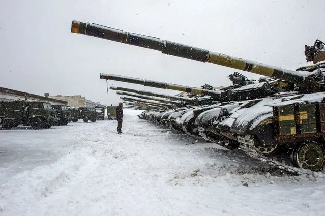 An Ukrainian Military Forces serviceman stands in front of tanks of the 92nd separate mechanized brigade of Ukrainian Armed Forces, parked in their base near Klugino-Bashkirivka village, in the Kharkiv region on January 31, 2022. The tanks have to restore their combat capability after completing a combat mission in war-torn eastern Ukraine. (Photo by Sergey Bobok/AFP Photo)