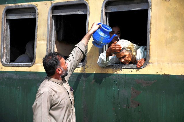 A woman, leaning out of a train window, receives water on her head to cool off during a hot and humid day at the Hyderabad Railway Station in Hyderabad, Pakistan on May 22, 2024. (Photo by Yasir Rajput/Reuters)