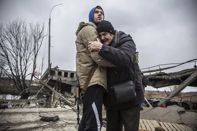 A Ukrainian Territorial Defence Forces member hugs a resident who leaves his home town following Russian artillery shelling in Irpin, on the outskirts of Kyiv, Ukraine, Wednesday, March 9, 2022. (Photo by Oleksandr Ratushniak/AP Photo)