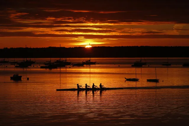 A quad scull of rowers begin their workout on Casco Bay as the sun starts to peak over Great Diamond Island, Wednesday, August 28, 2019, in Portland, Maine. Calm winds and flat water made for ideal conditions for the Portland Community Rowing Association's final outing of the year. (Photo by Robert F. Bukaty/AP Photo)