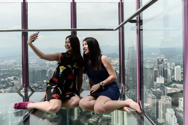 Ng Sin Nee (L) and Lee Shin May (R) from Malaysia take pictures with the panoramic view of the city from the Sky Box at KL Tower, the world's seventh tallest telecommunications tower, in Kuala Lumpur on May 24, 2016. Officially opened on May 20, the Sky Box has been the latest attraction for tourists arriving to the Malaysian capital. It stands 300 metres above ground and can fit six people at any one time, and offers spectacular views of the Kuala Lumpur skyline, including the iconic Petronas Twin Towers. (Photo by Mohd Rasfan/AFP Photo)