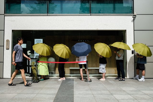 A man walks past customers queueing outside a restaurant as they hold umbrellas to provide shade from the sun in Seoul on July 3, 2024. (Photo by Anthony Wallace/AFP Photo)