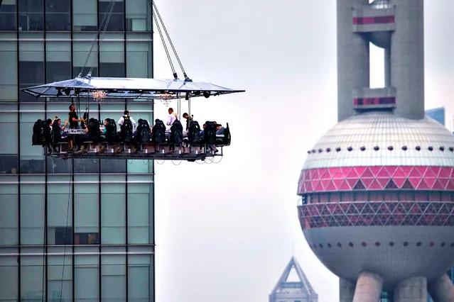 Diners are suspended from a crane as they enjoy a meal organized by the “Dinner in the Sky” over Lujiazui Financial District in Shanghai on June 27, 2014. (Photo by AFP Photo/Stringer)