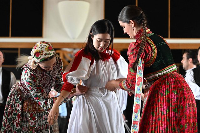 Members of the Hungarian National Dance Ensemble dress a member of the South Korean Mutdance dance collective in a Hungarian national costume before their joint rehearsal in Budapest, Hungary, on June 14, 2023. The South Korean group, that has female members only, will perform their programme later at the 10th International Theatre Olympics in Hungary. (Photo by Attila Kisbenedek/AFP Photo)