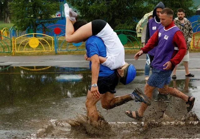 A man carries his wife over an obstacle while competing in the Wife Carrying Championship to mark City Day in Krasnoyarsk, Siberia, Russia, June 25, 2016. (Photo by Ilya Naymushin/Reuters)