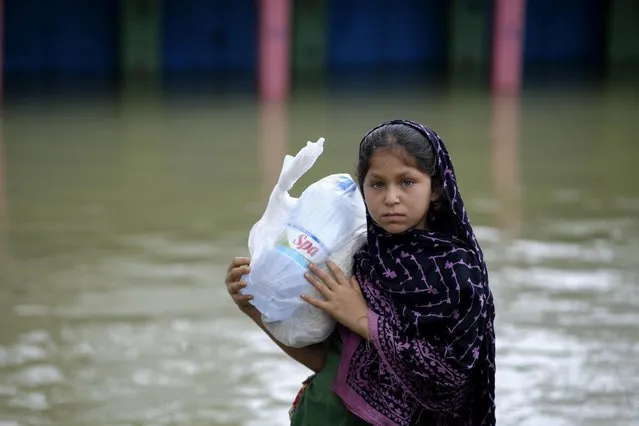 A flood-affected girl walks with relief material at Companygonj in Sylhet, Bangladesh, Monday, June 20, 2022. (Photo by Mahmud Hossain Opu/AP Photo)