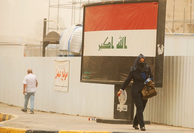 A woman covers her face as she walks past a national flag in Baghdad with white dust covering the Iraqi capital and surrounding areas on June 13, 2022 for the tenth time since mid-April. – Iraq temporarily closed Baghdad airport due to crippling duststorms, the latest in a country that has warned climate change poses an “existential threat”. (Photo by Ahmad Al-Rubaye/AFP Photo)
